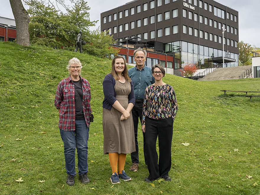 Fyra personer på en gräsmatta framför ett universitet. Foto